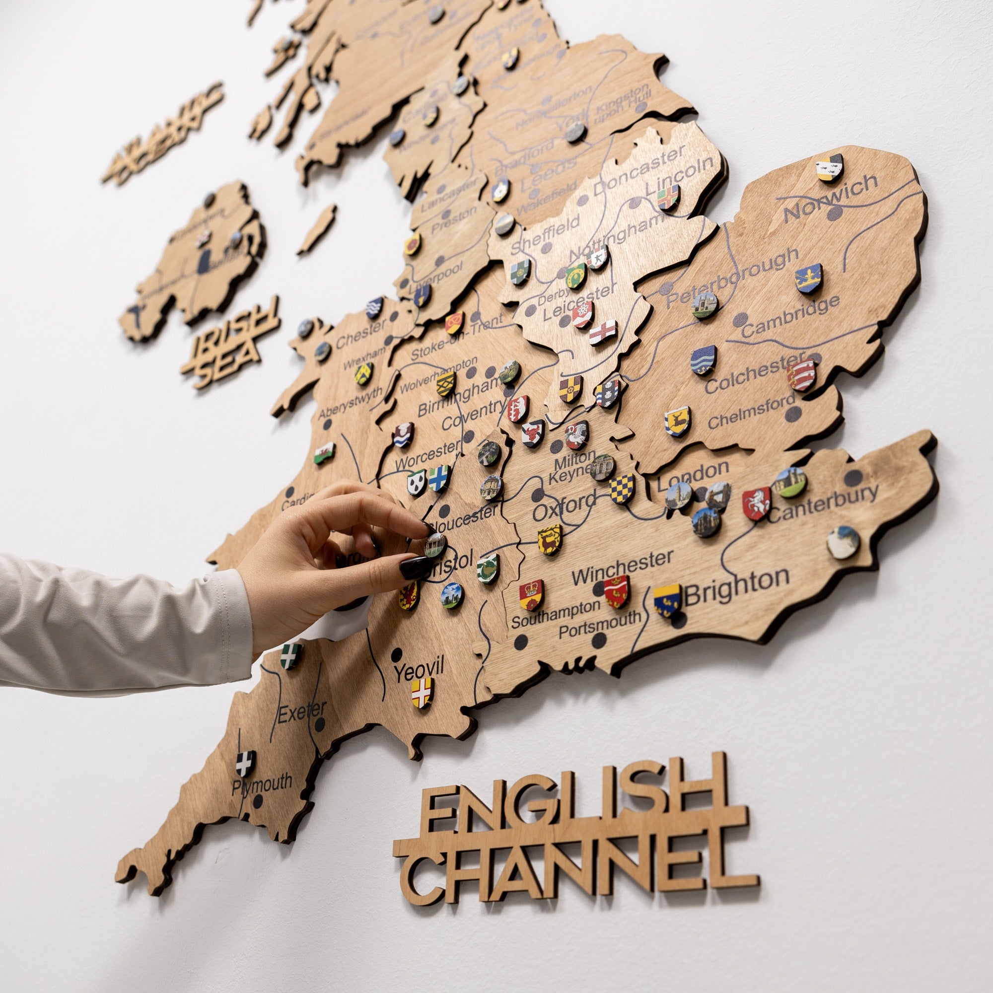Wooden map of England with pins and a hand interacting with it on a white background