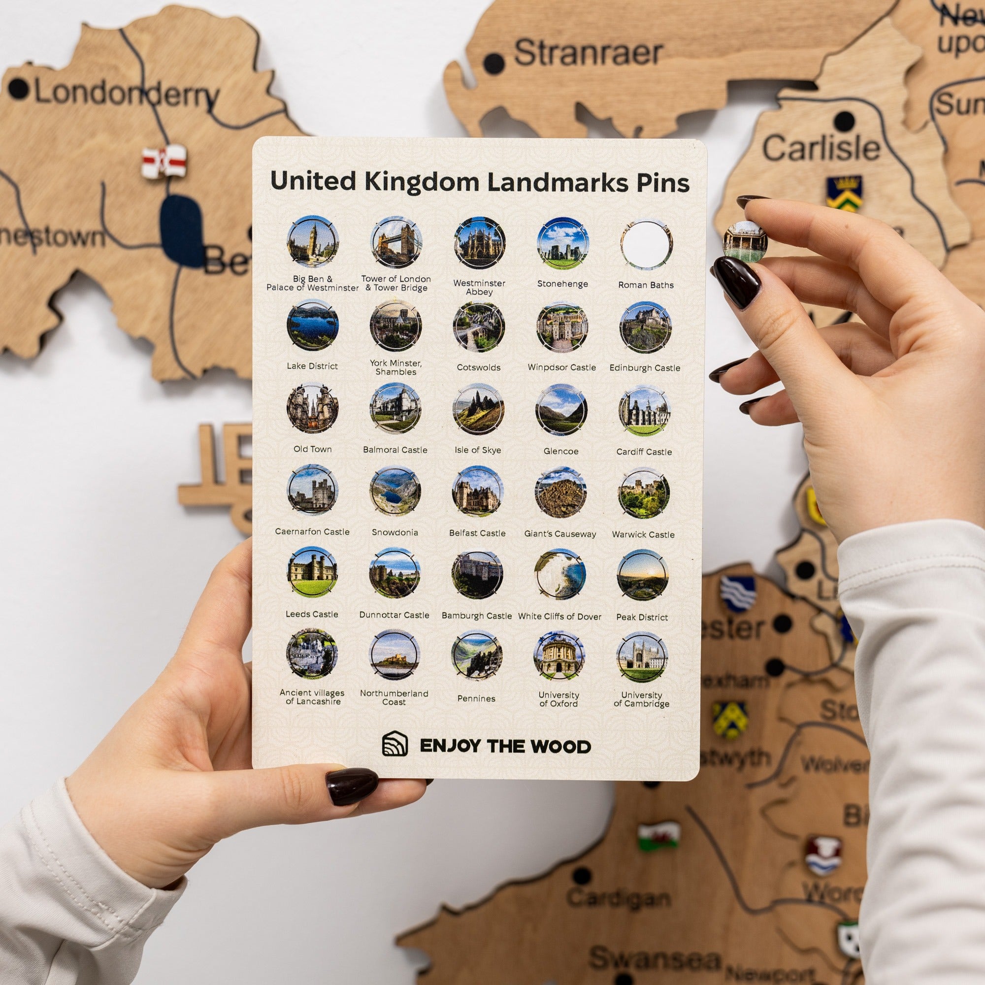 Hand holding a card with United Kingdom landmarks pins against a wooden map background