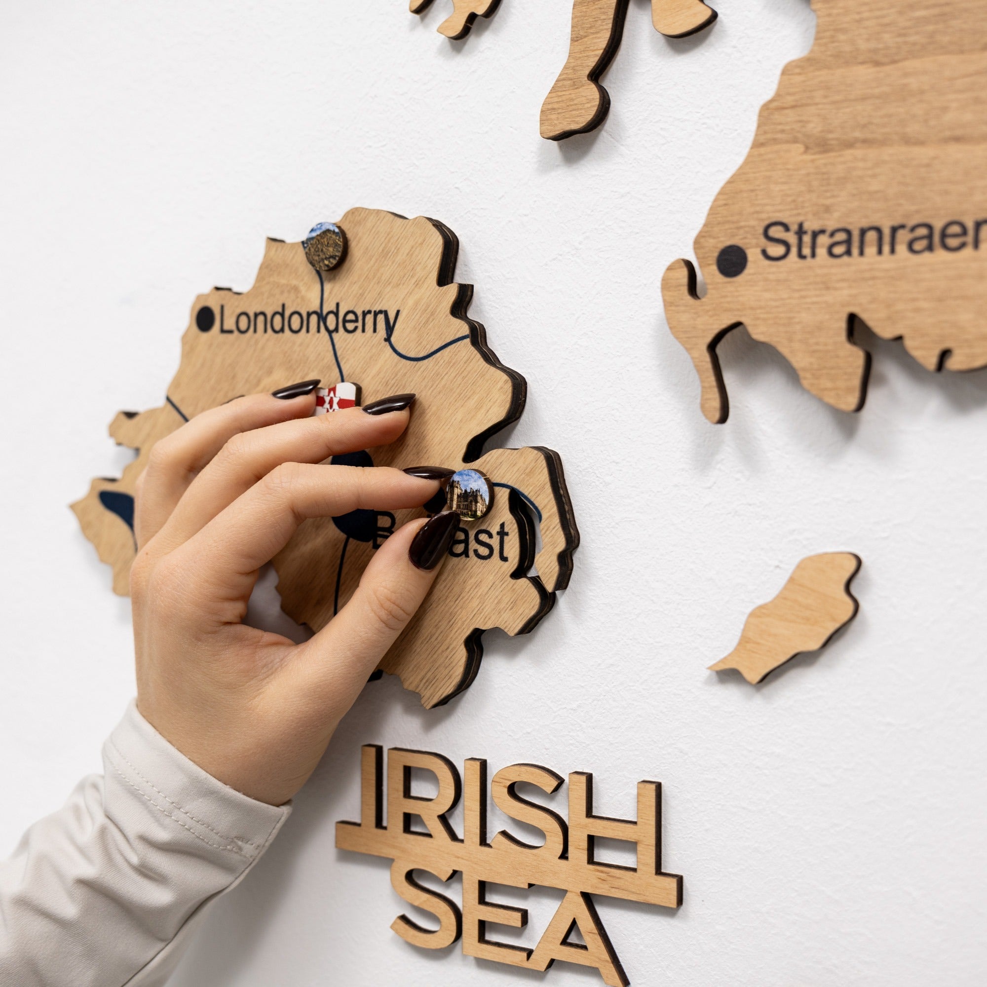 Wooden map of Ireland with a hand placing a piece on a white background
