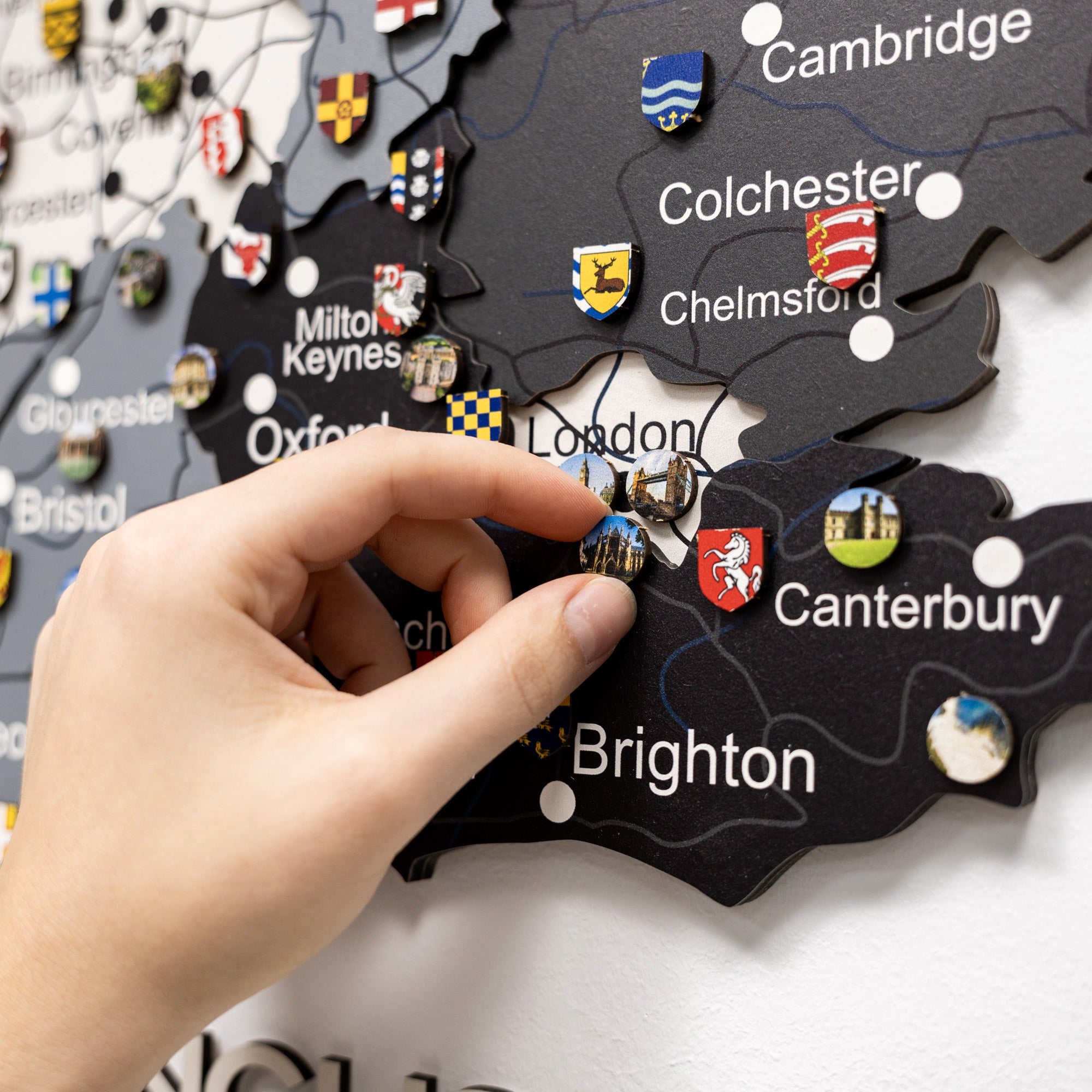 Map of England with city names and pins, hand placing a pin on London.