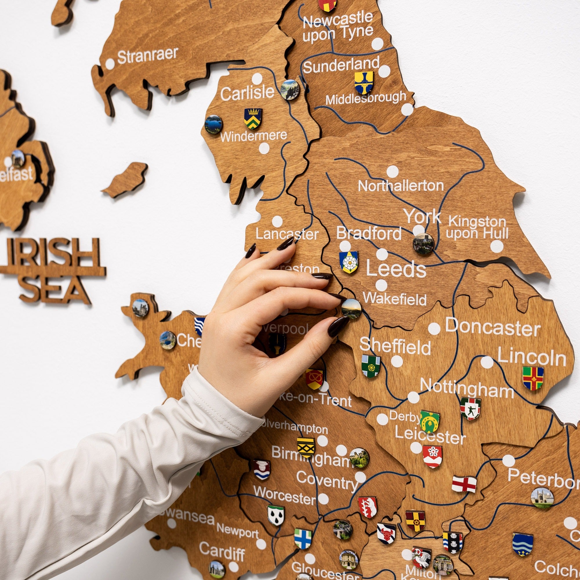 Wooden map of the United Kingdom with cities labeled, hand placing a flag on 'Leeds'.