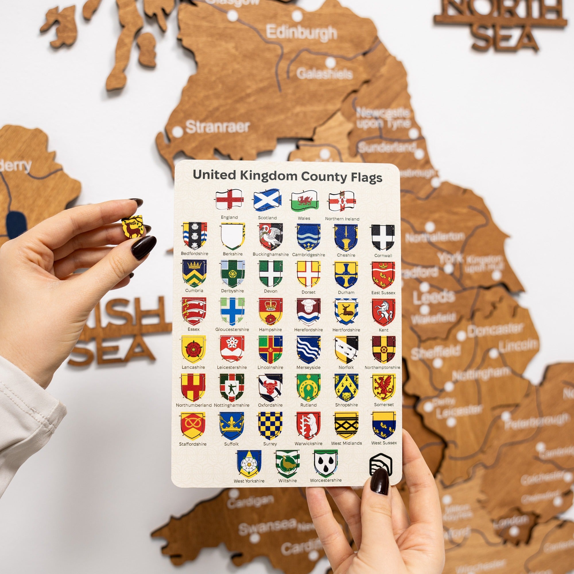 Person holding a card with United Kingdom county flags against a wooden map background