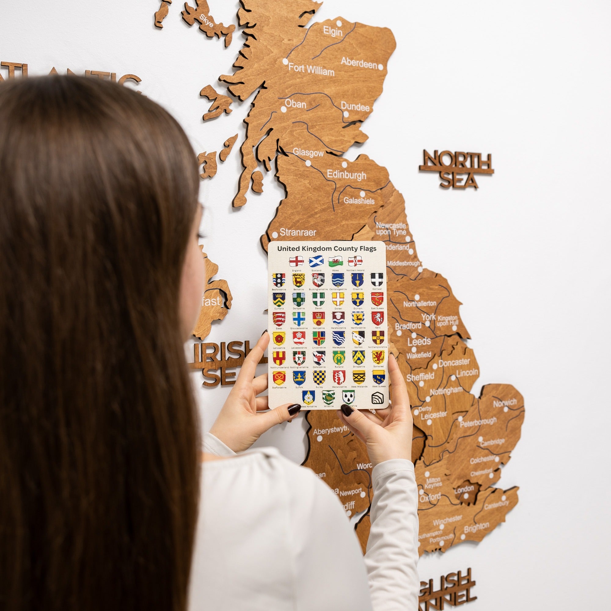 Person holding a phone with UK county flags in front of a wooden map of Scotland.