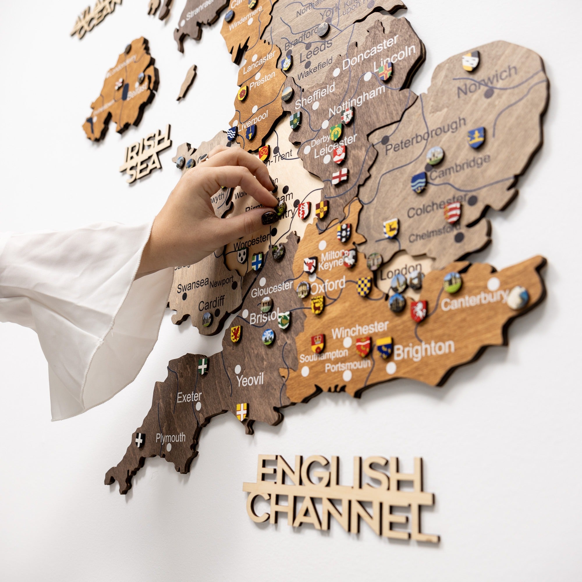 Wooden map of England with pins and a hand interacting with it on a white background