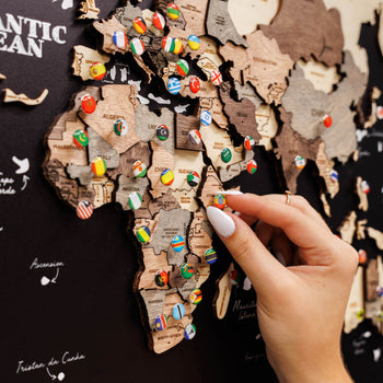 Hand placing a wooden puzzle piece on a world map with colorful pins.