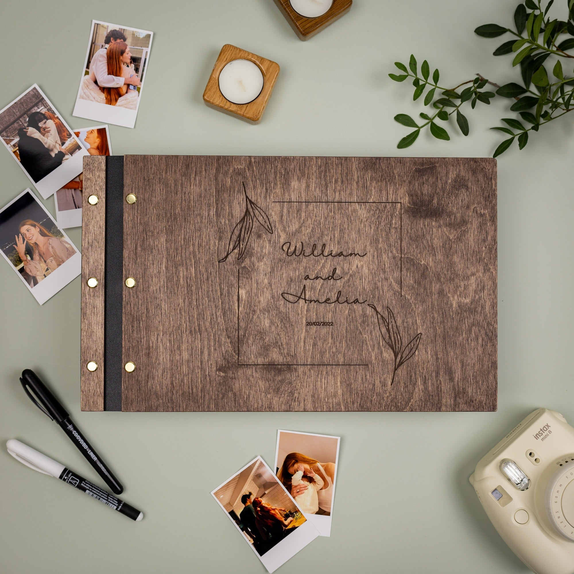 Wooden photo album with engraved text, surrounded by photos and a camera on a light green surface.