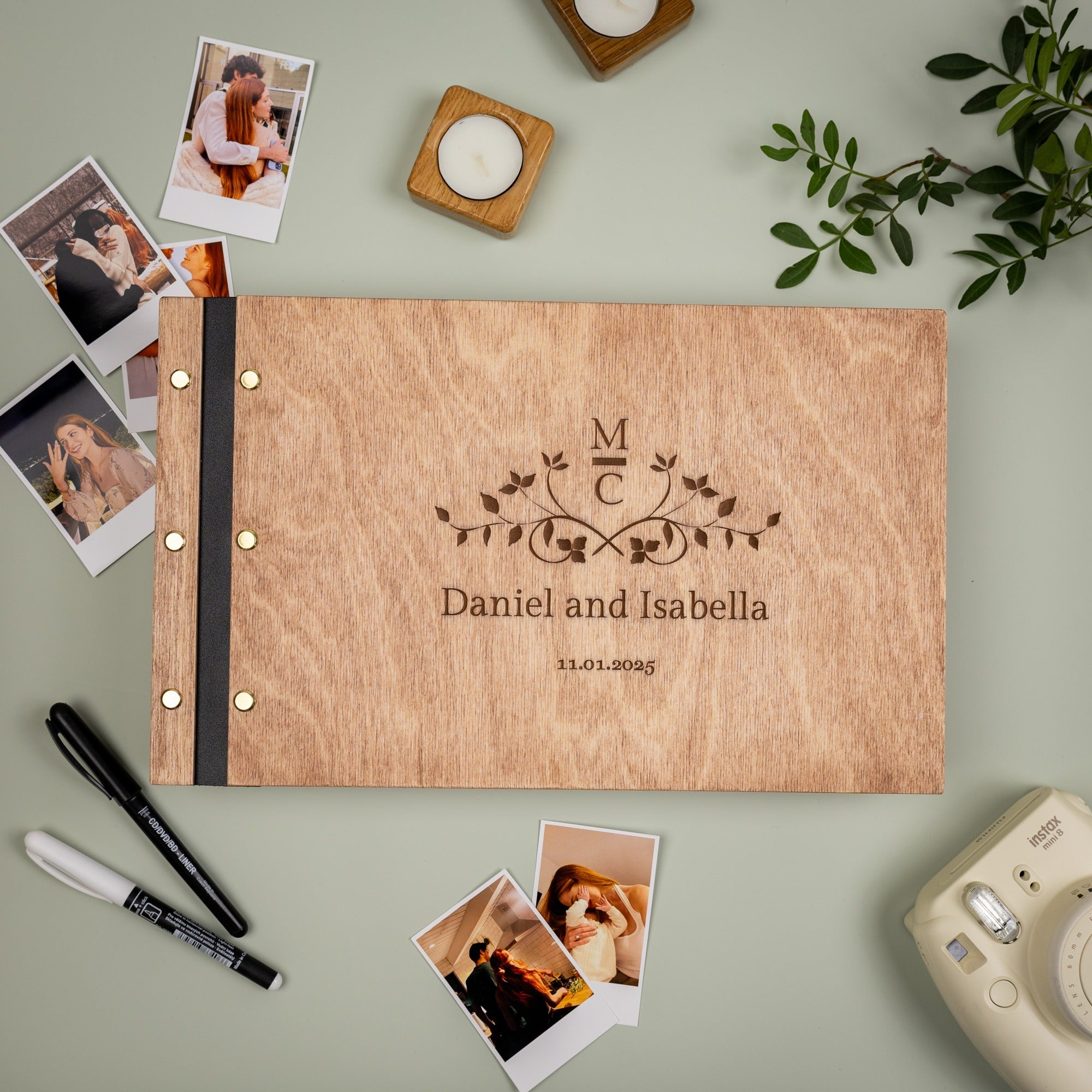 Wooden photo album with engraved initials and names, surrounded by photos and a camera on a light green background.
