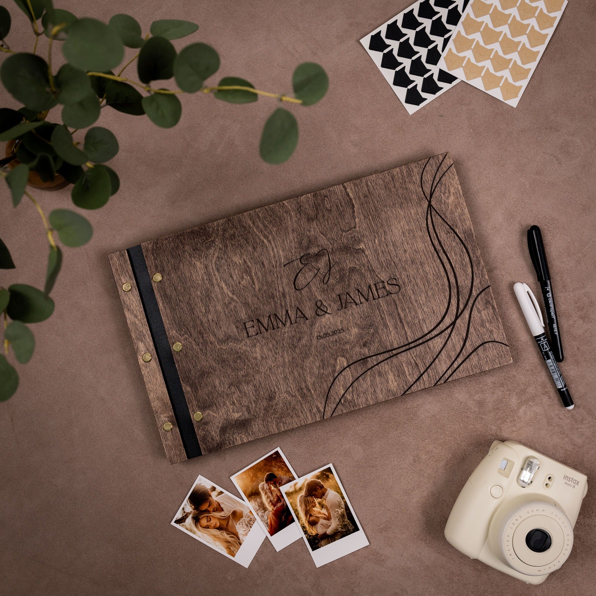 Personalized photo album with 'Emma & James' on a brown surface with photos and a camera.