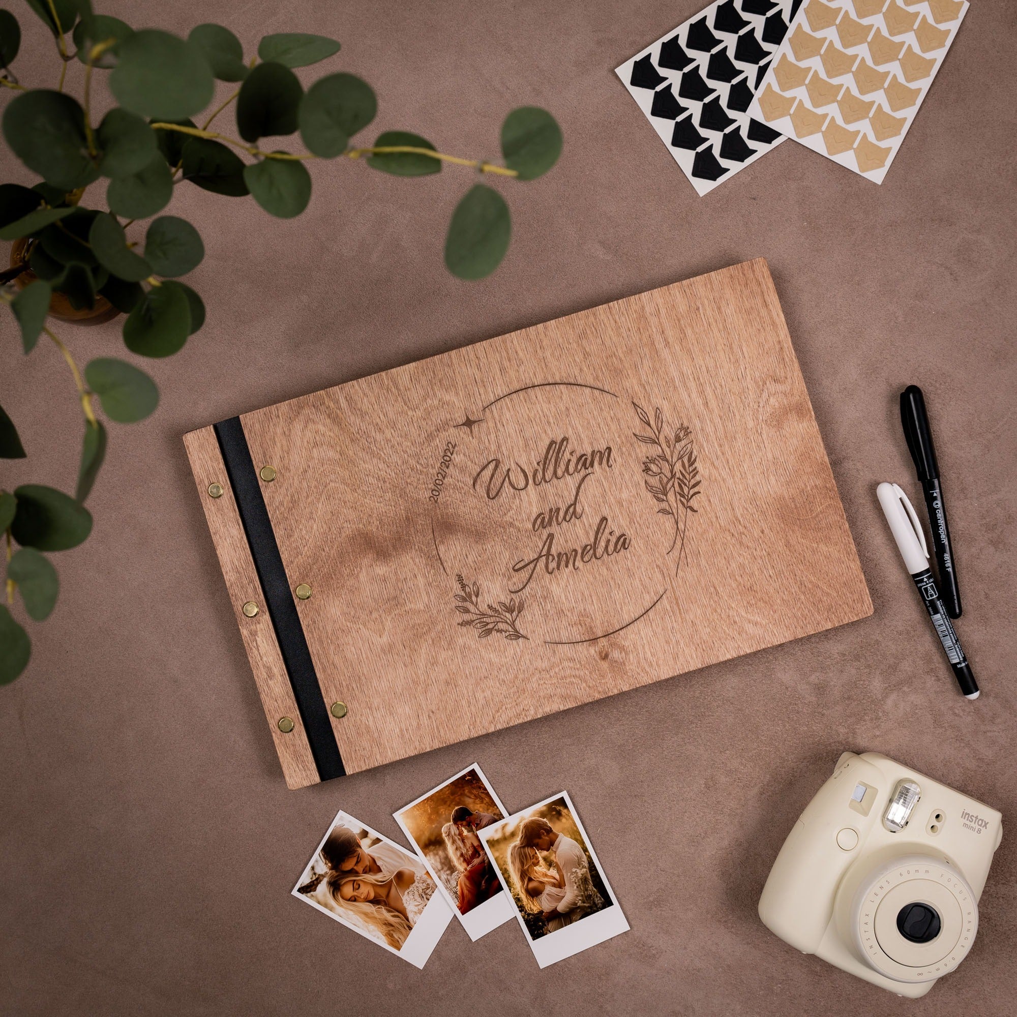 Wooden photo album with engraved names, photos, and a camera on a brown surface.